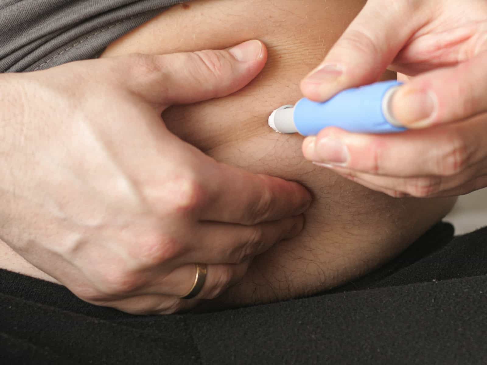 Close-up of a person administering a semaglutide injection into their abdomen with a blue pen injector, highlighting its use in weight loss and diabetes management.